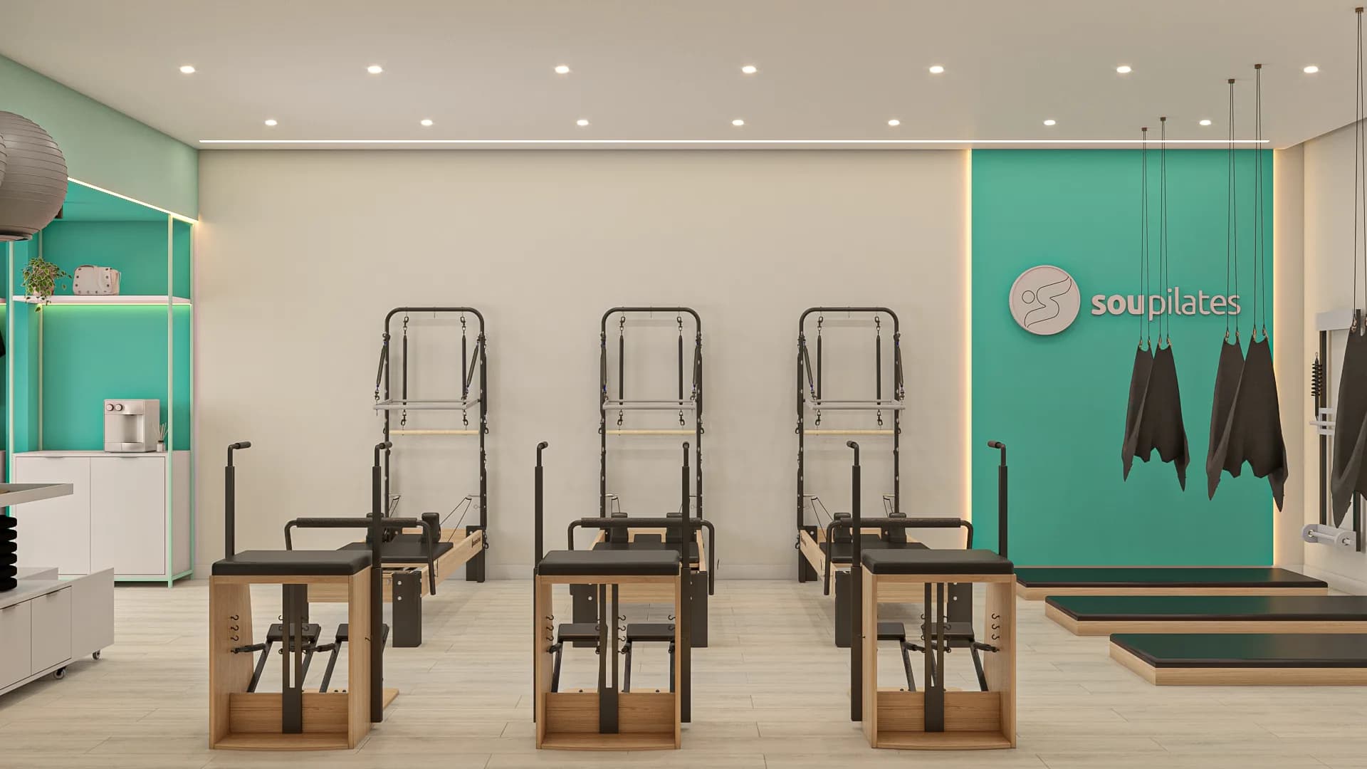 Sala de pilates da Sou Pilates vista de frente, com a fileira de cadillacs, faixas de suspensão e a parede verde com o logotipo.