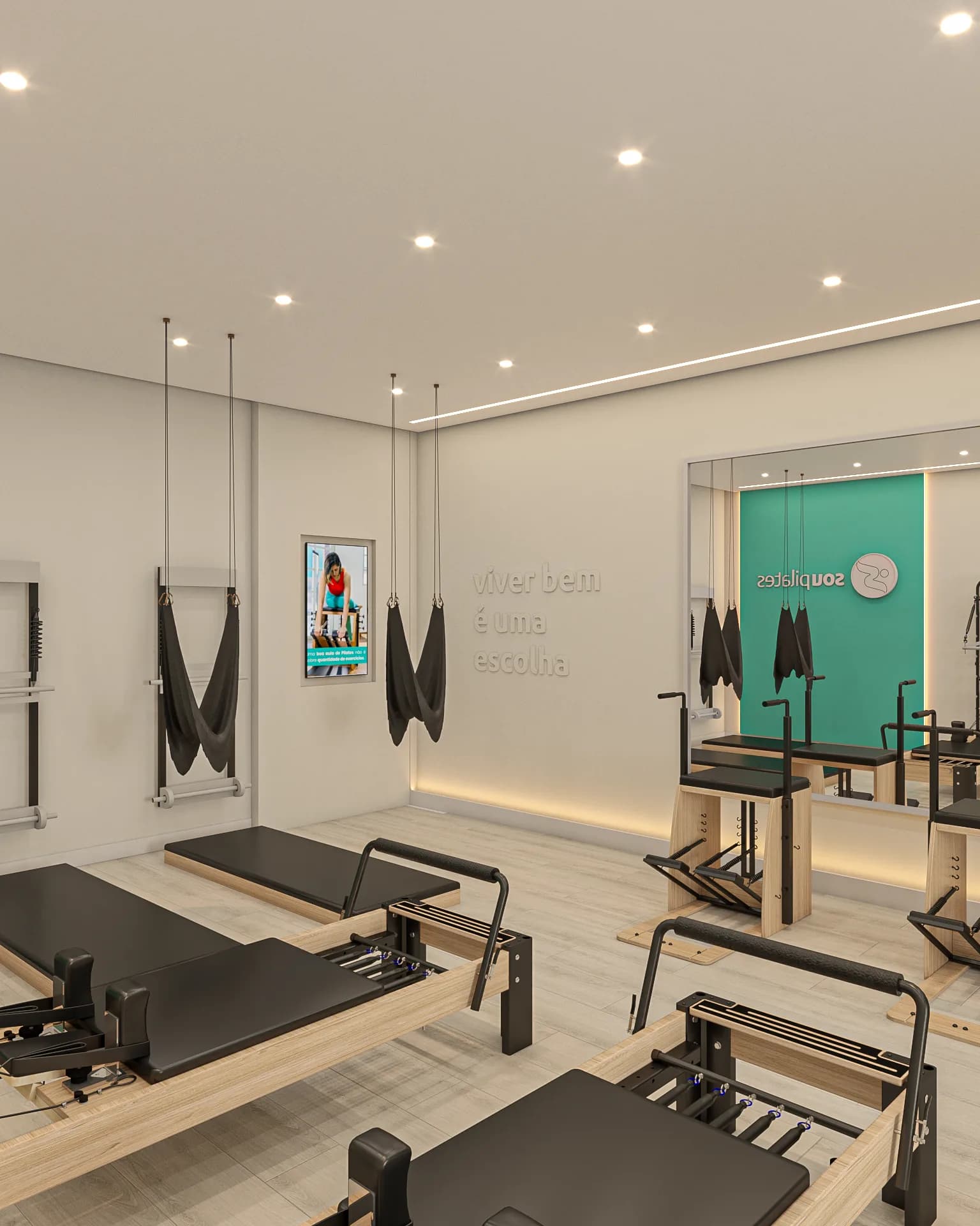 Sala de pilates da Sou Pilates com reformers em primeiro plano, faixas de suspensão e a TV na parede ao fundo.