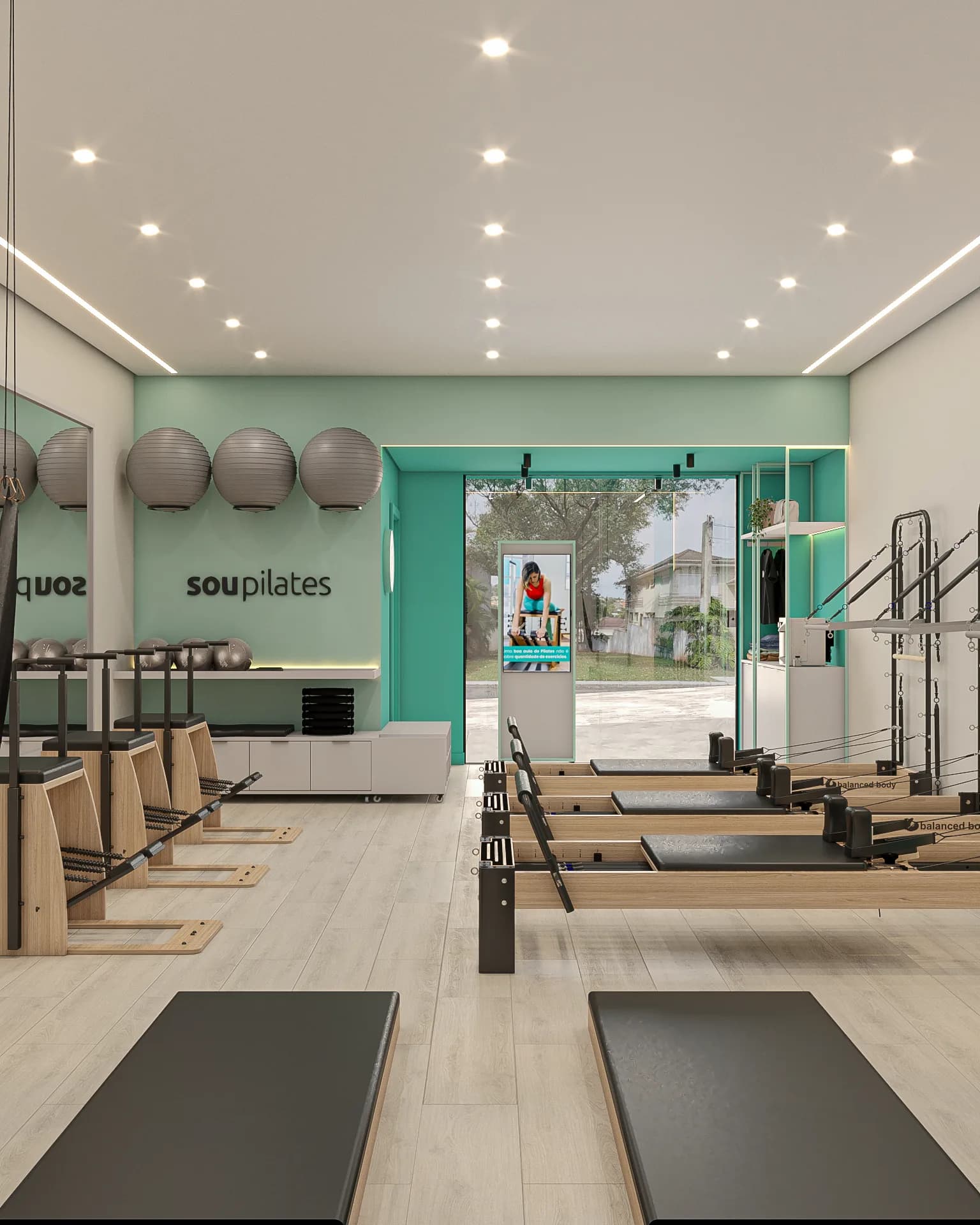 Sala de pilates da Sou Pilates vista do fundo, com colchonetes, reformers, bolas suíças e a vitrine para a rua.