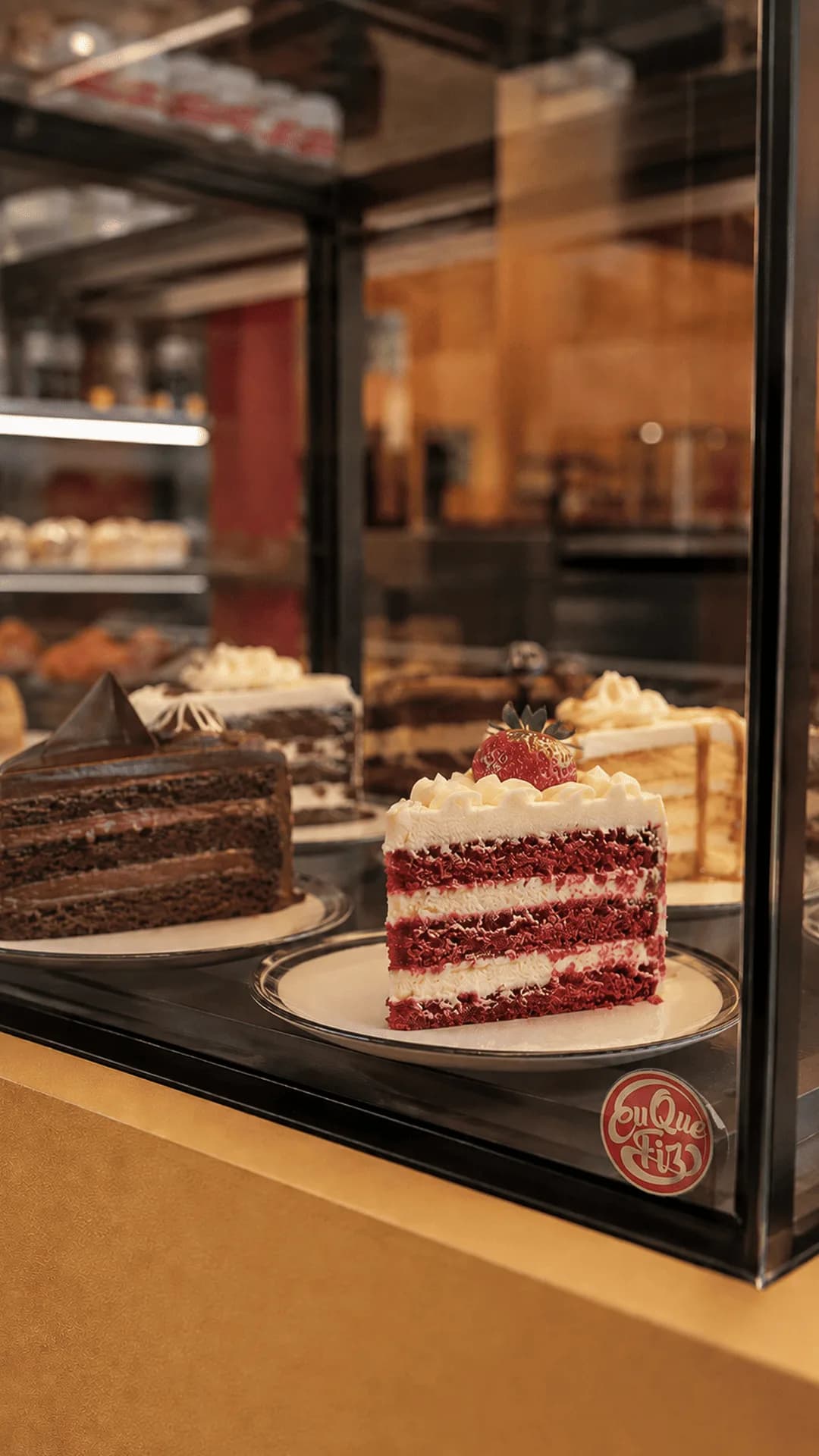 Vitrine de confeitaria exibindo fatias de bolo artesanal Red Velvet com morango e bolo de chocolate.