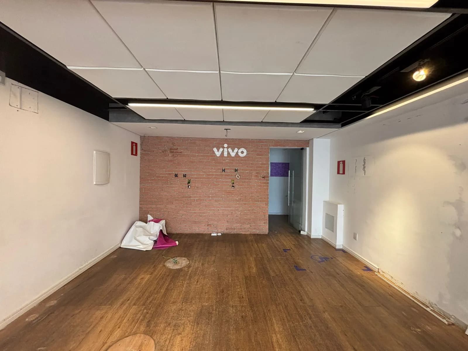 Antes da Gigi Bambini: salão vazio da antiga loja, com piso de madeira e parede de tijolos aparentes ao fundo.