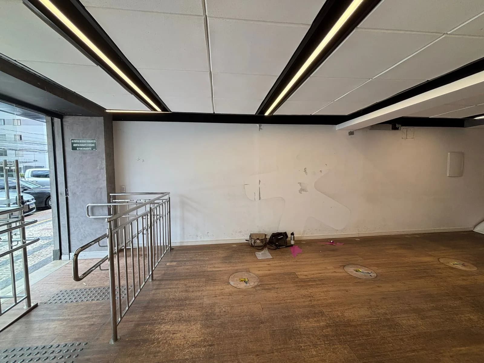 Antes da Gigi Bambini: entrada da antiga loja com guarda-corpo de inox, piso tátil e parede branca vazia.