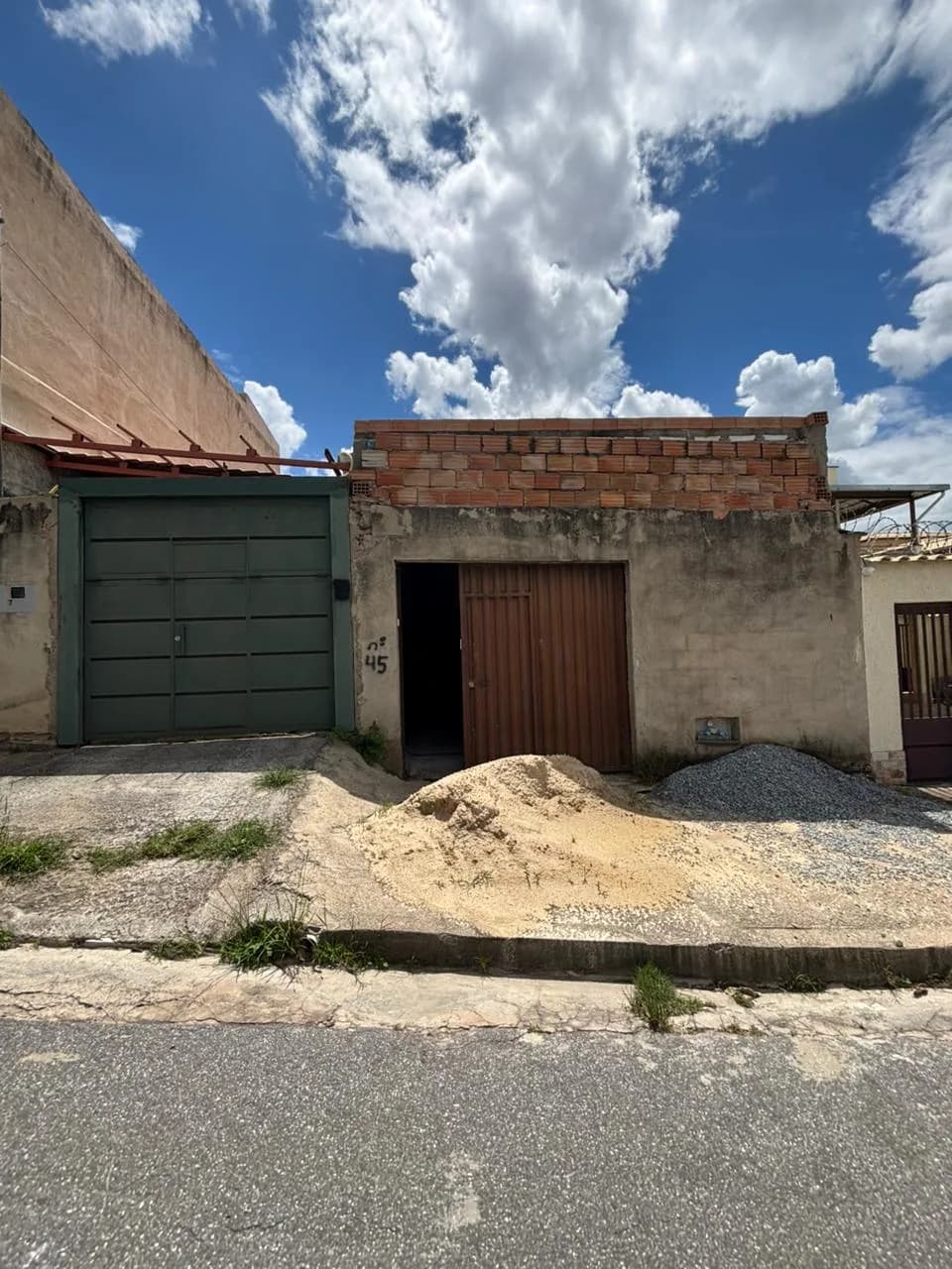 Antes da obra da Sou Pilates: o imóvel visto da rua, com portão verde e monte de areia na calçada.