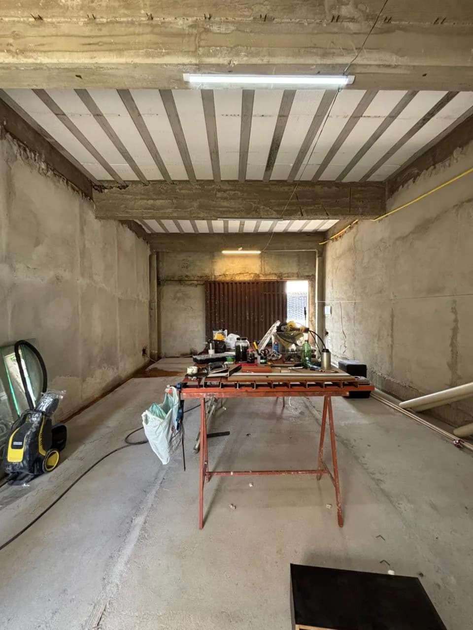 Antes da obra da Sou Pilates: fundo do salão em obra, com bancada de serralheria e porta de madeira.