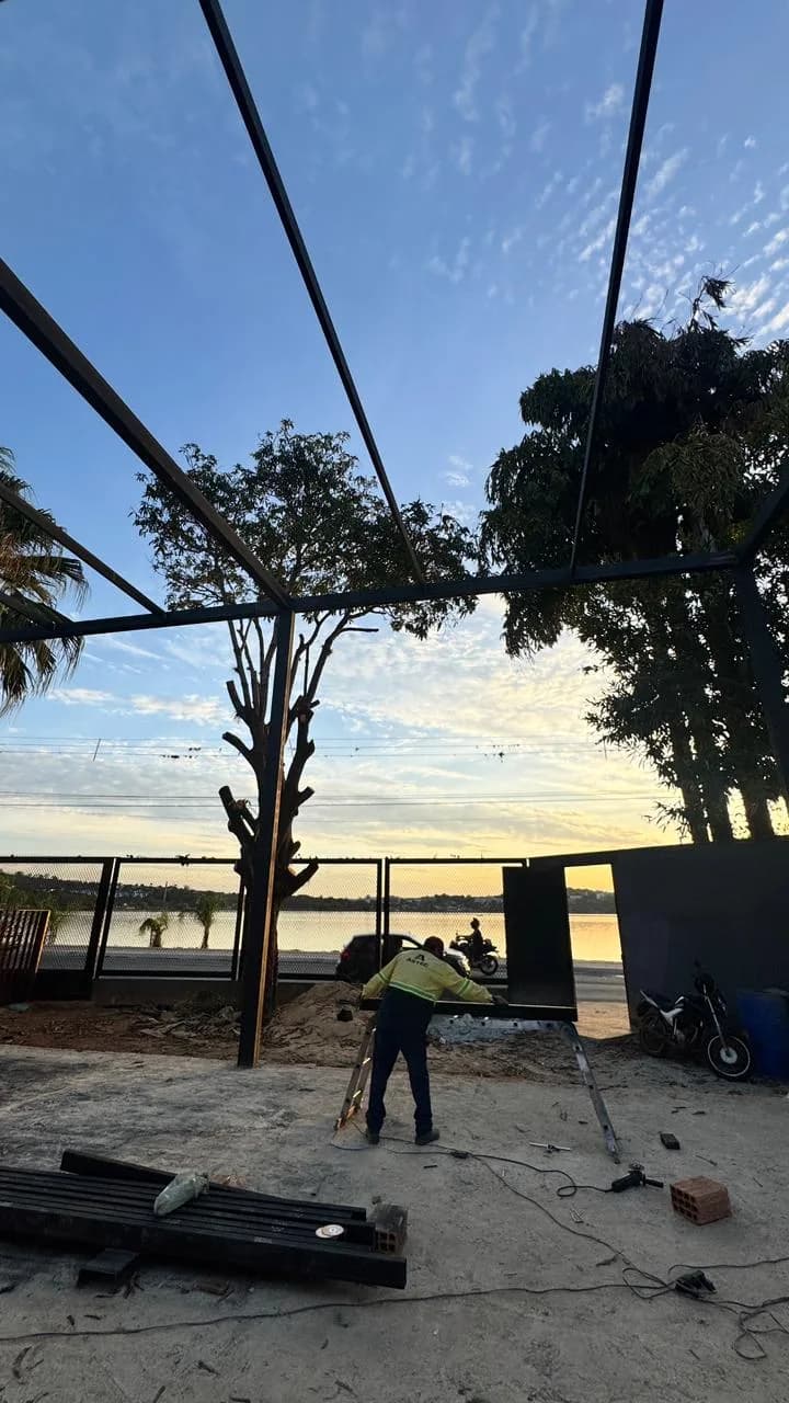 Antes da Altimetria: vigas metálicas do telhado sobre o terreno em obra, com um operário trabalhando ao fim da tarde.