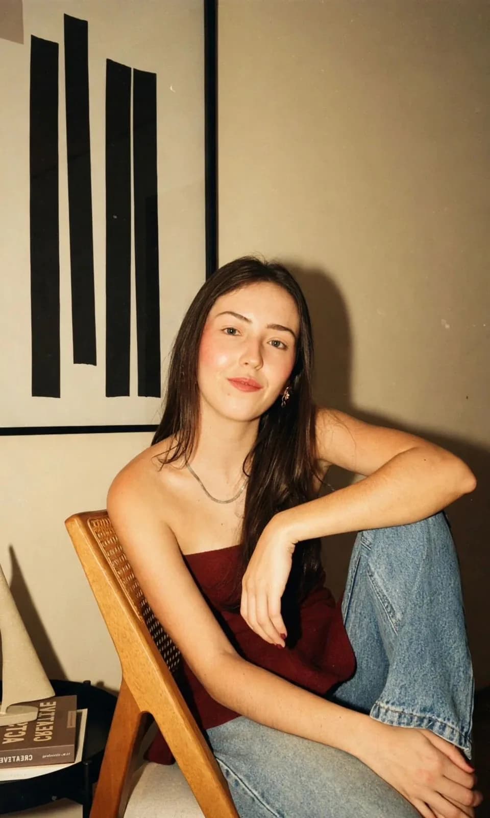 Esther Sousa, arquiteta e urbanista, fundadora da Distinto Arquitetura, sentada numa cadeira de madeira e palhinha diante de um quadro de faixas pretas.